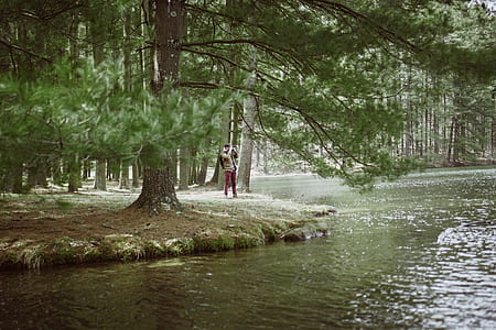 man standing beside body of water near green trees during daytime thumbnail
