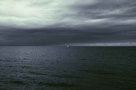 sailboat in the middle on the ocean under gloomy skies thumbnail