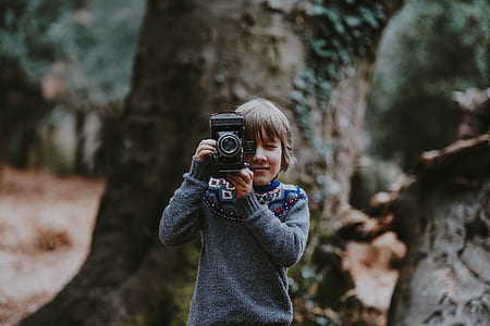 shallow focus photography of boy holding camera during daytime thumbnail