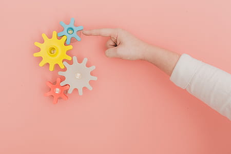 Finger turning colorful toy gears on peach color wall thumbnail