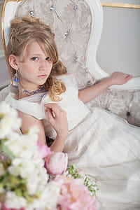 blonde haired girl wearing white dress sitting on tufted grey chair thumbnail