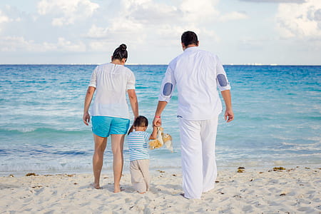 mother, father, and child walking on sea shore during daytime thumbnail