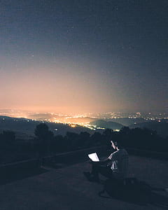 portrait photography of man sitting in front of mountains while using laptop thumbnail