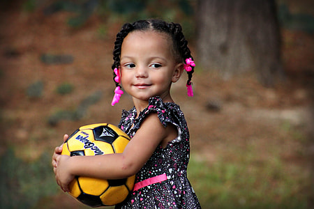 girl in white, pink and black floral sleeveless dress holding yellow and black soccer ball at daytime thumbnail