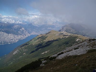 green grass covered mountains overlooking body of water and white cloudy sky thumbnail