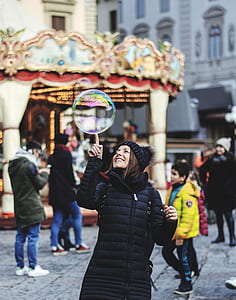 smiling woman putting bubble on top of her right index finger thumbnail