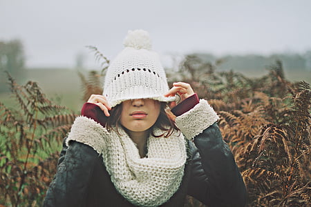 woman covering her eyes with her knitted cap beside brown leaf bush selective focal photo during daytime thumbnail