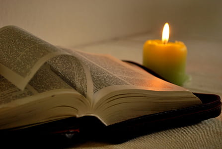 lighted yellow candle near opened book thumbnail