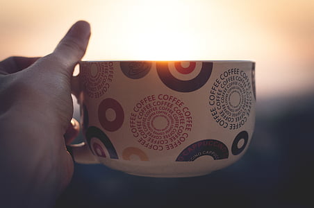 shallow focus photo of person holding white, red, and yellow ceramic mug thumbnail