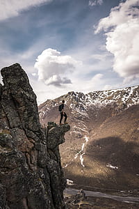 person standing on cliff under white clouds and blue sky during daytime thumbnail
