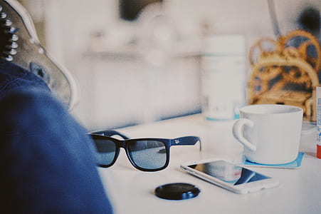 black Ray Ban Wayfarer sunglasses near white iPhone and white ceramic cup on table thumbnail
