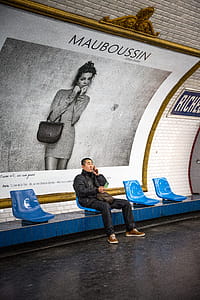 Man Sitting on Blue Chair in Front of Mauboussin Signage thumbnail