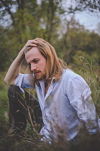 selective focus photography of man wearing white and blue collared button-up dress shirt sitting on green grass field during daytime thumbnail