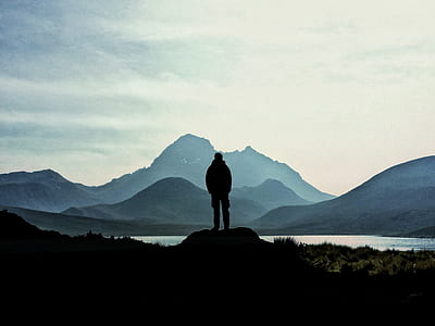 silhouette man standing on rock facing mountaing thumbnail