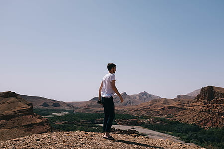 man standing on ground across rocky mountains during daytime thumbnail
