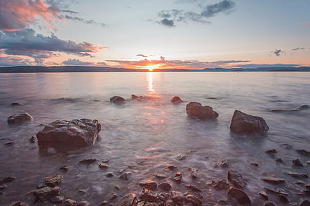 body of water near rocks during golden hour thumbnail