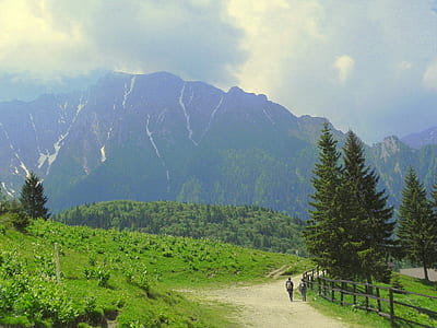 2 Person Walking Beside Grass Field Near Mountain thumbnail