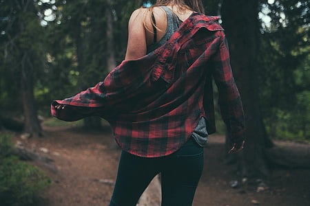 woman removing black and red sport shirt while walking near trees thumbnail
