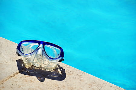 clear swimming goggle on gray concrete pavement near body of water thumbnail