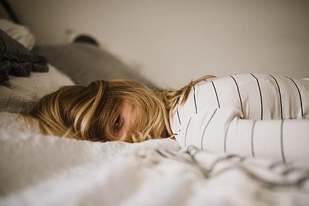 woman in white and black striped top laying on white textile during daytime thumbnail