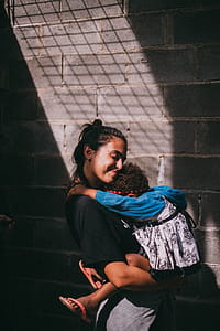 Woman Holding Girl Beside Gray Wall thumbnail