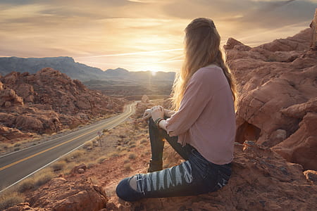 woman in pink 3/4-sleeved blouse and blue denim distressed jeans sitting in front of road during daytime thumbnail