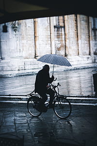 person bicycling while holding umbrella near wall thumbnail