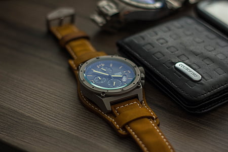 round chronograph watch beside black leather bi-fold wallet on wooden surface thumbnail