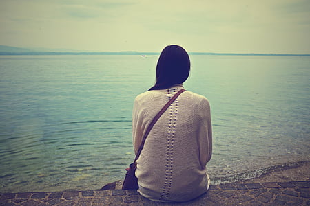 woman sitting on brown concrete pavement near ocean at daytime thumbnail