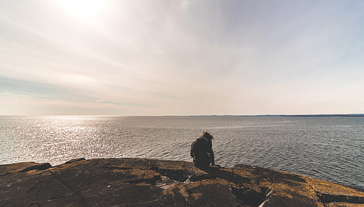 Person Sitting on Stone in Front of Sea Water thumbnail
