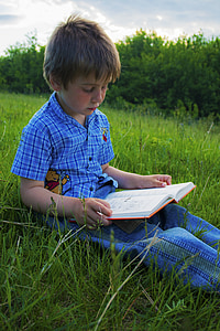 boy sitting on green grass field while reading book during daytime thumbnail