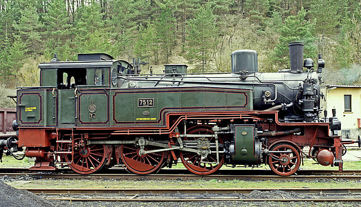 green and red steam engine near yellow house and green trees at daytime thumbnail