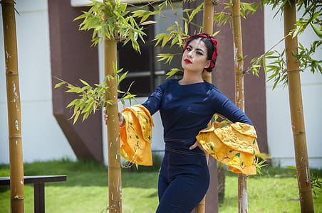 Woman Wearing Blue Long-sleeved Shirt While Leaning on Bamboo Grass thumbnail