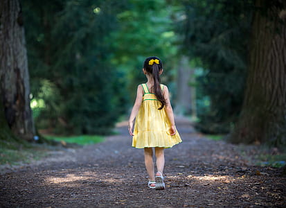 girl in yellow dress standing between trees pathway thumbnail