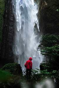 time lapse photography of man standing in front of waterfall thumbnail