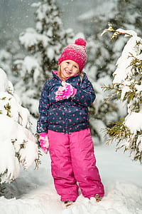 girl standing on snow between trees smiling while taking her a picture thumbnail