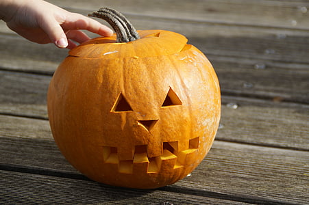 person touching jack-o'-lantern on brown wooden surface thumbnail