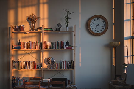 books on shelf near round wall clock next to window thumbnail