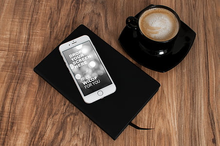 silver iPhone 6 on top of black notebook near black ceramic coffee mug with saucer thumbnail