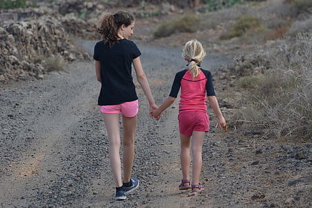 two girls walking on dusty road near grass thumbnail