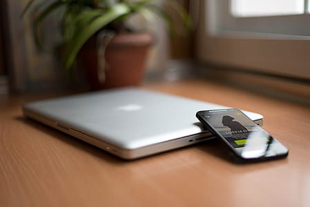 Smartphone Beside Silver Macbook on Brown Wooden Table With Potted Plant in the Background thumbnail