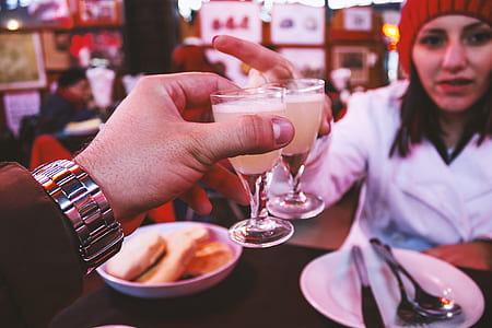 Man Wearing Silver Link Watch Holding a Glass Containing White Liquid in Front of a Woman thumbnail