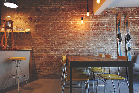 brown wooden dining table with yellow padded chairs near brick wall \ thumbnail