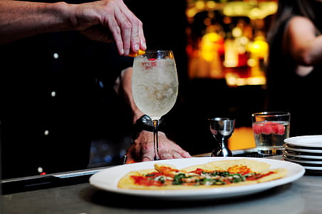 person holding wine glass' lip on table beside pizza on plate thumbnail