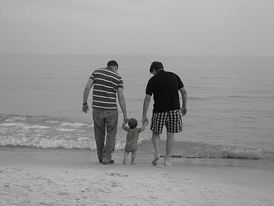 grayscale photo of two men guiding a child to walk on seashore thumbnail