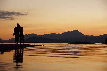 silhouette of couple standing beside body of water at golden hour thumbnail