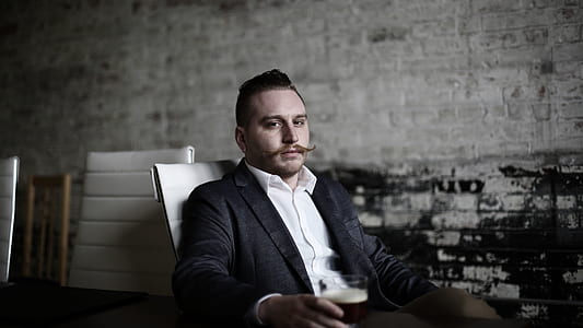 man sitting on chair holding glass of black liquid thumbnail