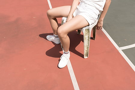 person wearing white shorts sitting on plastic chair beside green court thumbnail