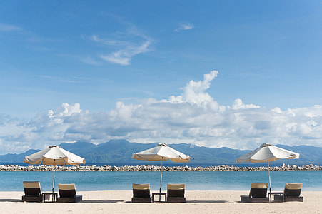 three white and black sun lounger with umbrellas facing sea thumbnail
