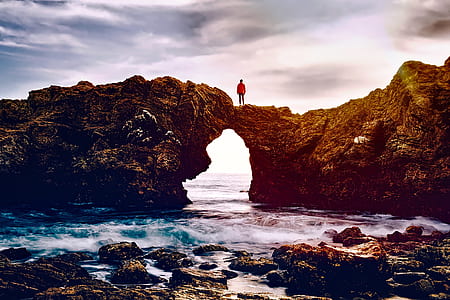 person standing on boulder rock in sea under clouds thumbnail